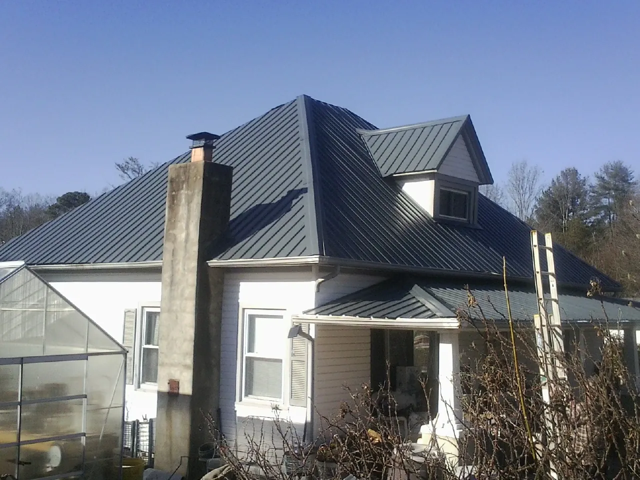 Dark blue standing seam metal roof on a white farmhouse with dormer — Slate & Tile Roof Repair by Roofing Brothers in Pine Bluff
