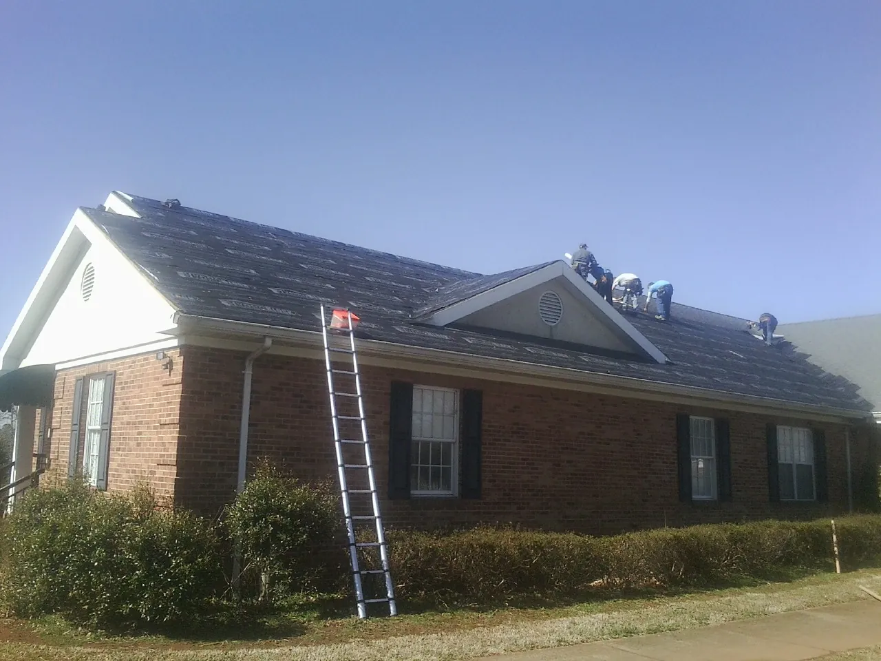 Crew tearing shingles off a brick ranch roof with a ladder set — Metal Roof Repair work by our crew in Pine Bluff