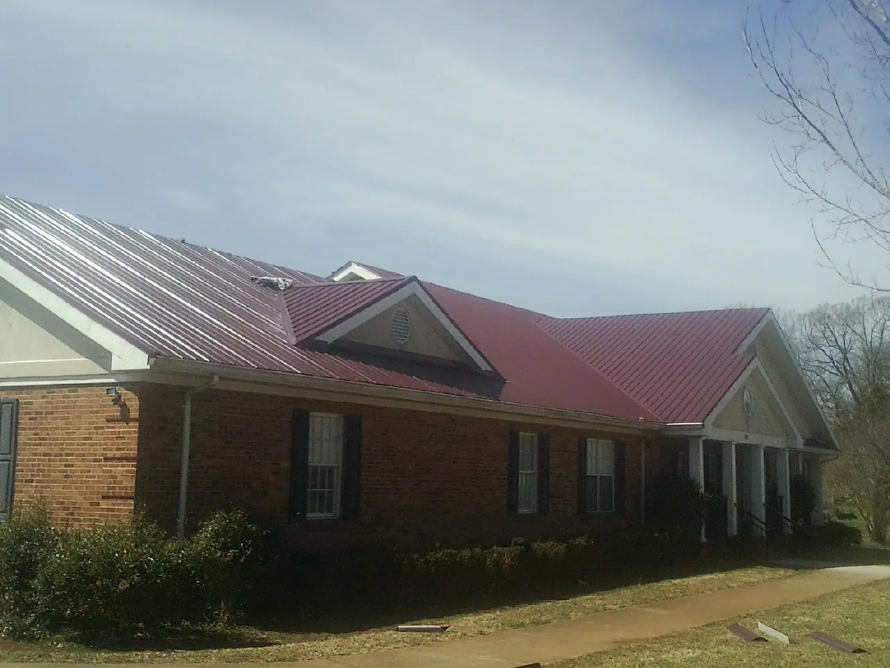 Red metal roof with gabled entries on a long brick building, from a Hail Damage Roof Repair job in Pine Bluff