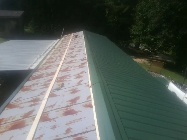 Old rusted panels beside newly installed green metal roofing — Wind Damage Roof Repair by Roofing Brothers in Pine Bluff