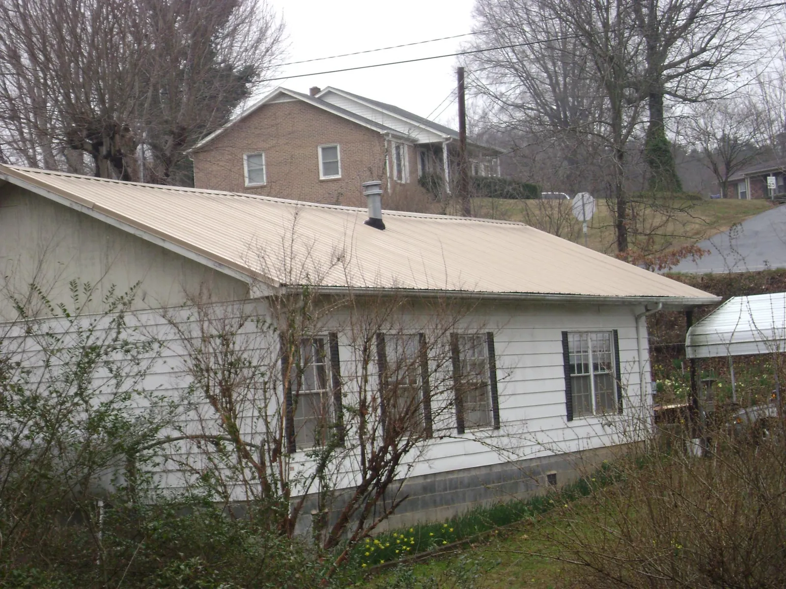 Tan metal roof on a white sided house set into a hillside — Commercial Roofing by Roofing Brothers in Pine Bluff